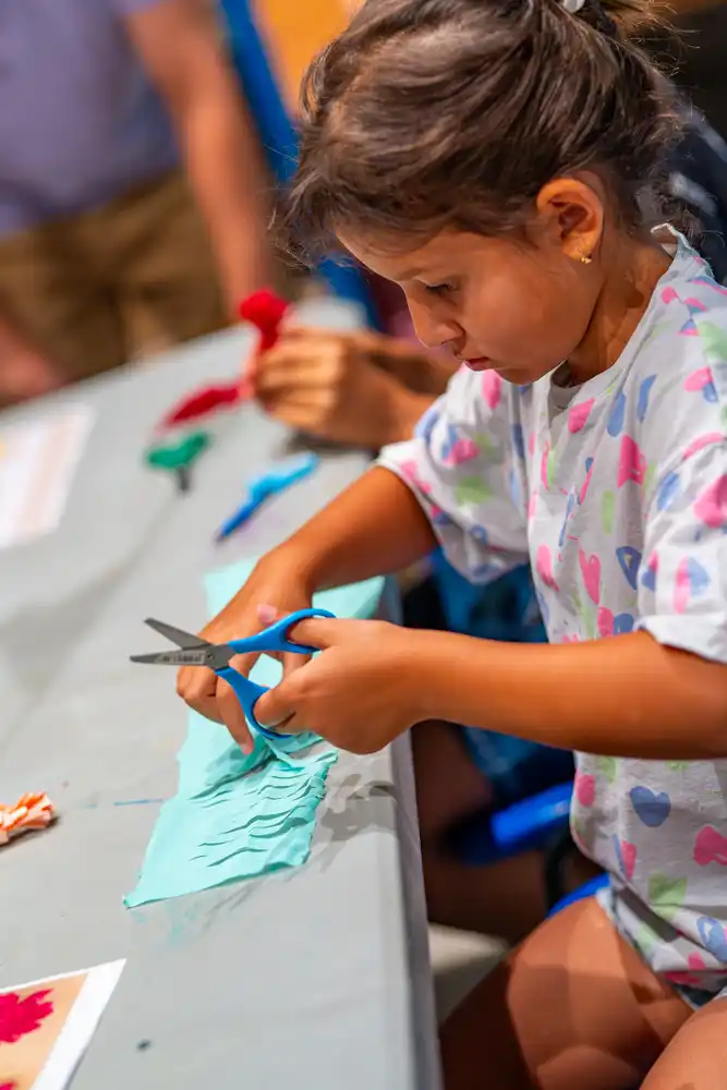 Enfant utilisant des ciseaux pour découper une bande de papier bleu lors d'un atelier créatif.