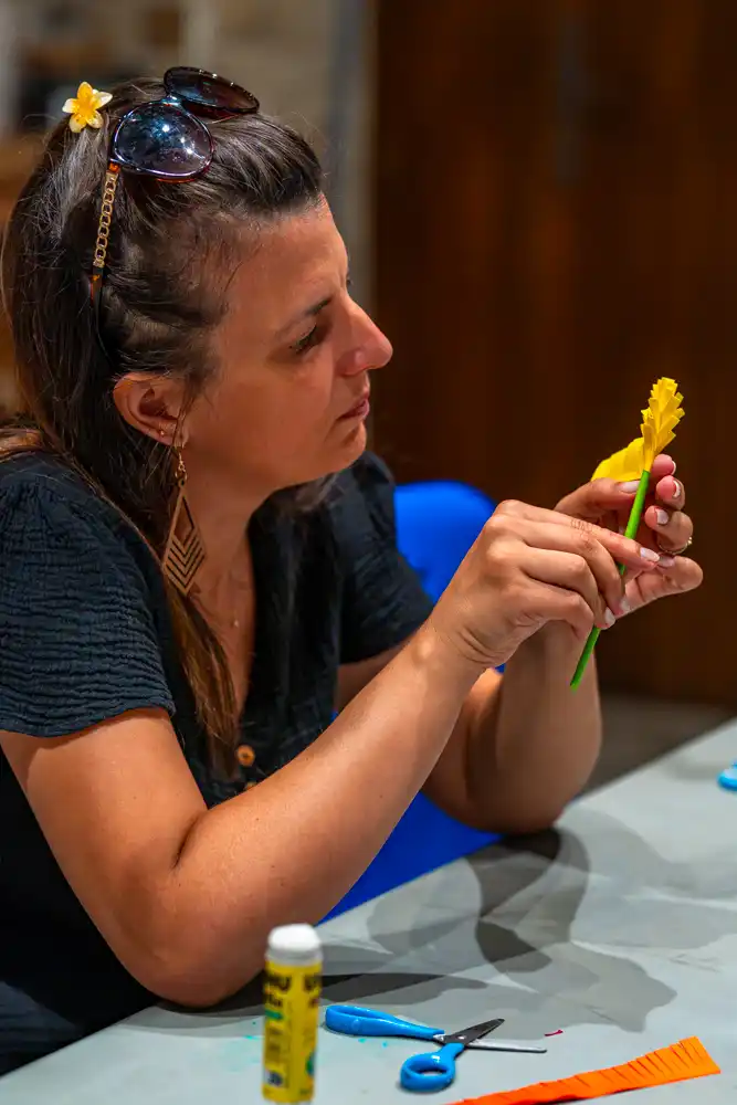 Une participante concentrée sur la confection d'une fleur en papier jaune lors d'un atelier créatif.