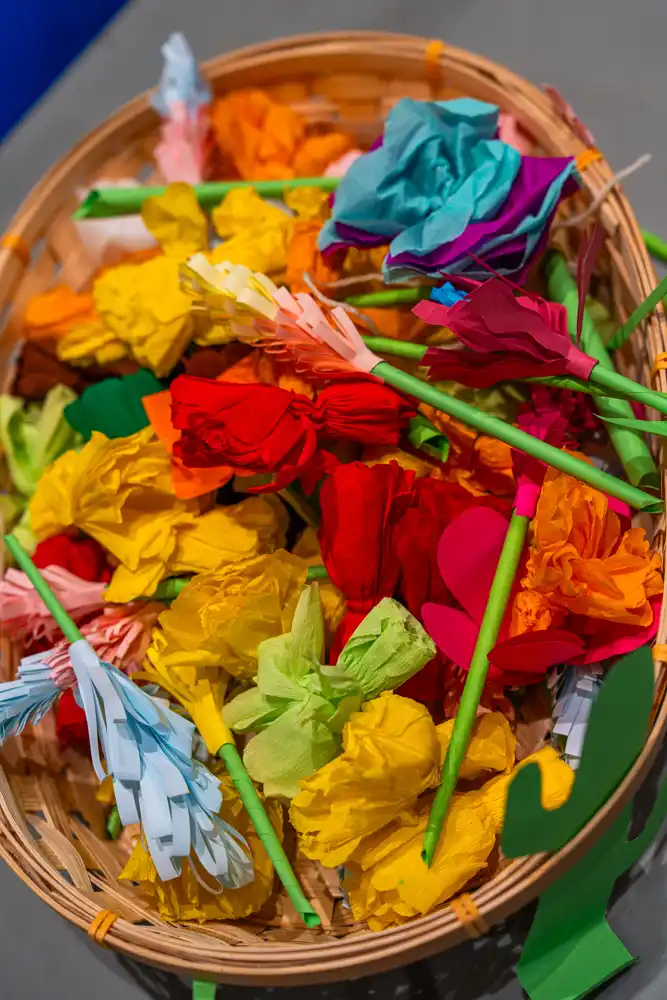 Panier en osier rempli de fleurs artisanales en papier crépon coloré, réalisées lors d'un atelier créatif.