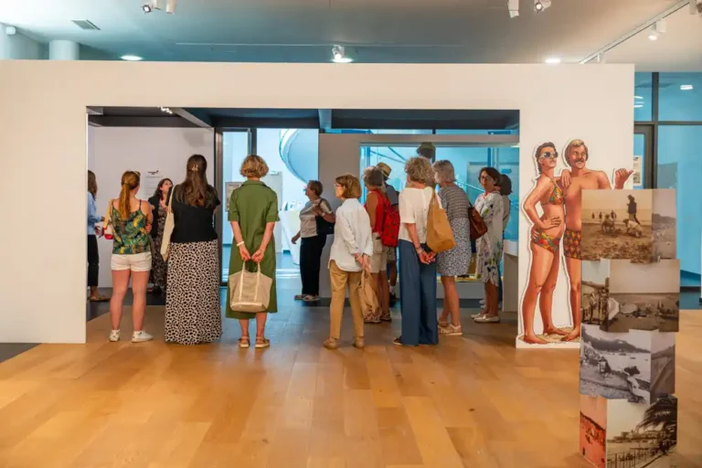 Visiteurs lors de la visite guidée de l'exposition sur l'histoire du tourisme dans le Var, à côté d'une silhouette en carton de baigneurs rétro.