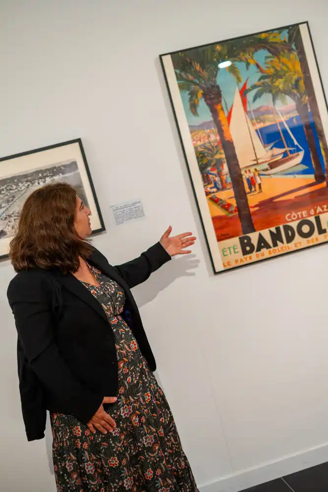 Une guide présente une affiche touristique vintage de Bandol lors de la visite de l'exposition sur l'histoire du tourisme dans le Var.