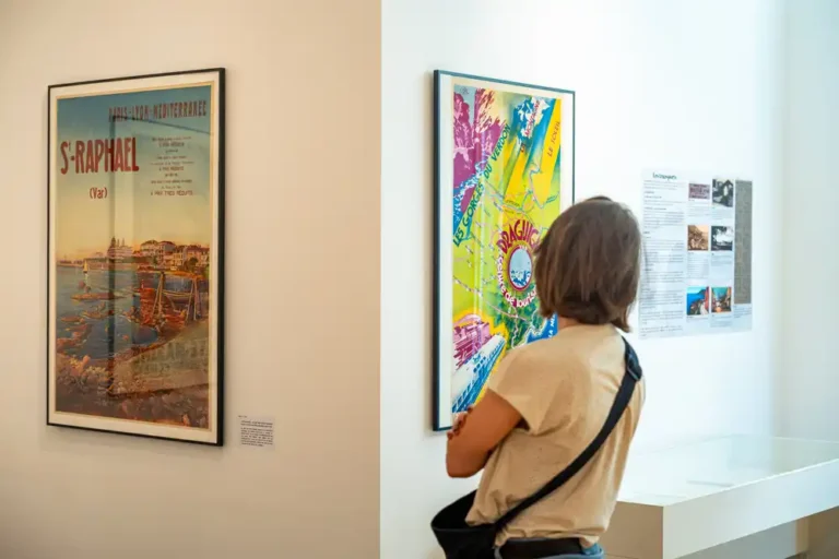 Visiteuse observant des affiches touristiques anciennes sur le Var lors de l'exposition aux Archives départementales.