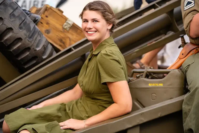 Une jeune femme souriante en tenue d'époque assise à bord d'un véhicule militaire lors du défilé de la Libération.