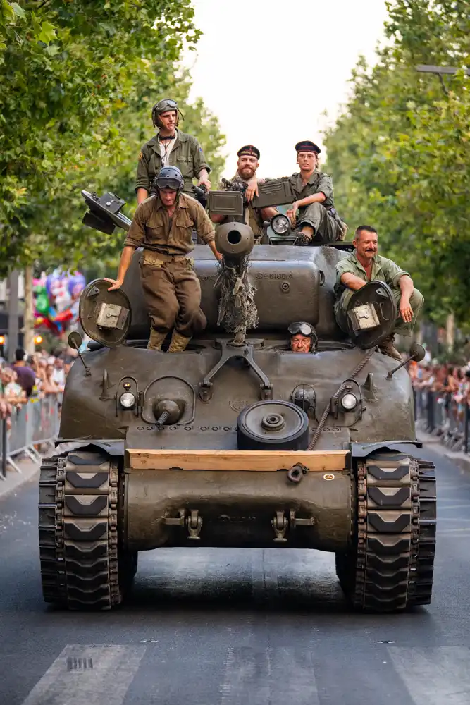 Char d'assaut d'époque circulant sur le boulevard Clemenceau lors du défilé de la Libération, avec des personnes en tenue militaire à son bord.