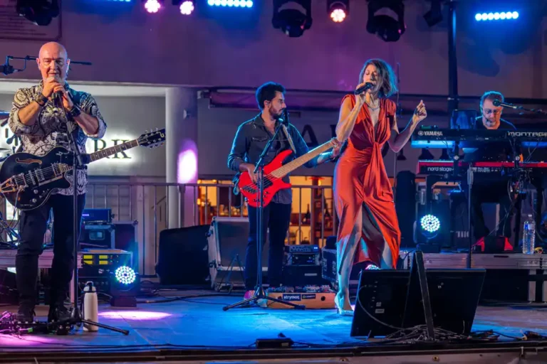 Groupe de musique sur scène lors du bal de la Libération, composé d'un guitariste-chanteur, d'un bassiste, d'une chanteuse en robe rouge et d'un claviériste.