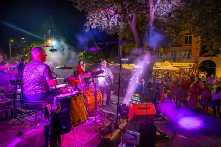Groupe de musique en concert sur une scène installée en extérieur lors du bal de la Libération, avec le public en arrière-plan.