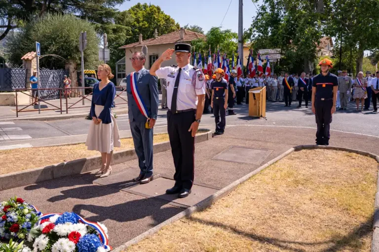 Cérémonie commémorative de la Libération de Draguignan : élus et représentants des corps constitués en tenue officielle saluent devant une stèle fleurie.