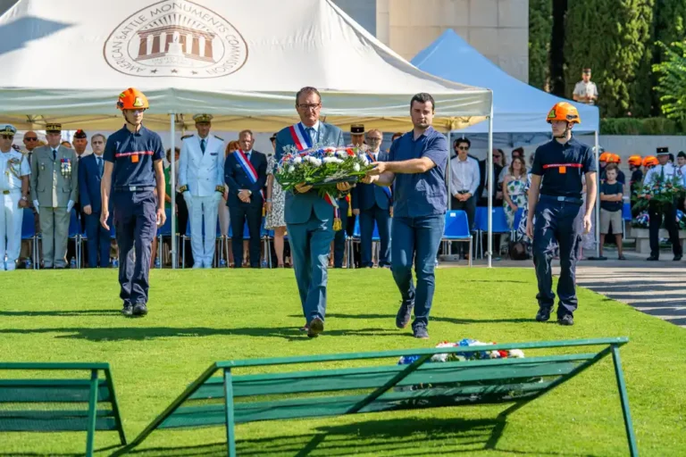 Richard Strambio, maire de Draguignan, accompagné d'un autre homme et de deux jeunes sapeurs-pompiers, dépose une gerbe de fleurs lors de la cérémonie de la Libération au cimetière américain Rhône.