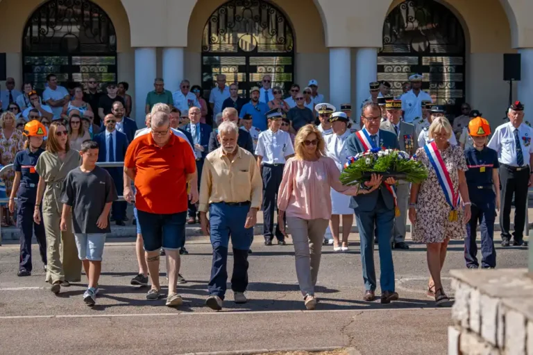 Cérémonie de commémoration de la Libération de Draguignan avec des élus portant une gerbe de fleurs, entourés de citoyens et de représentants officiels.