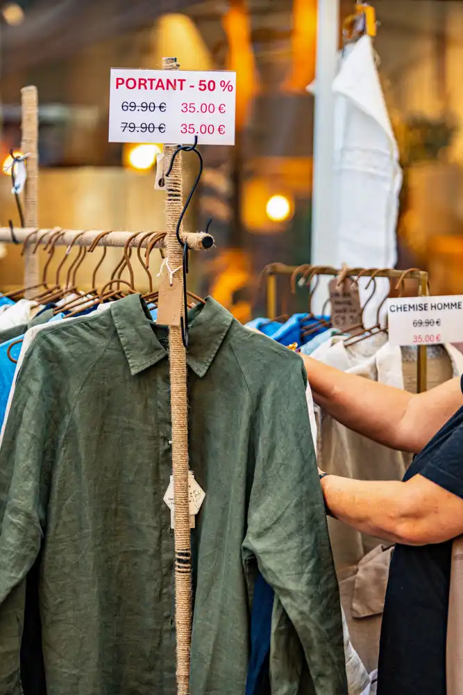 Portants de vêtements avec des étiquettes de réduction affichant -50 % sur les prix initiaux lors de la braderie.