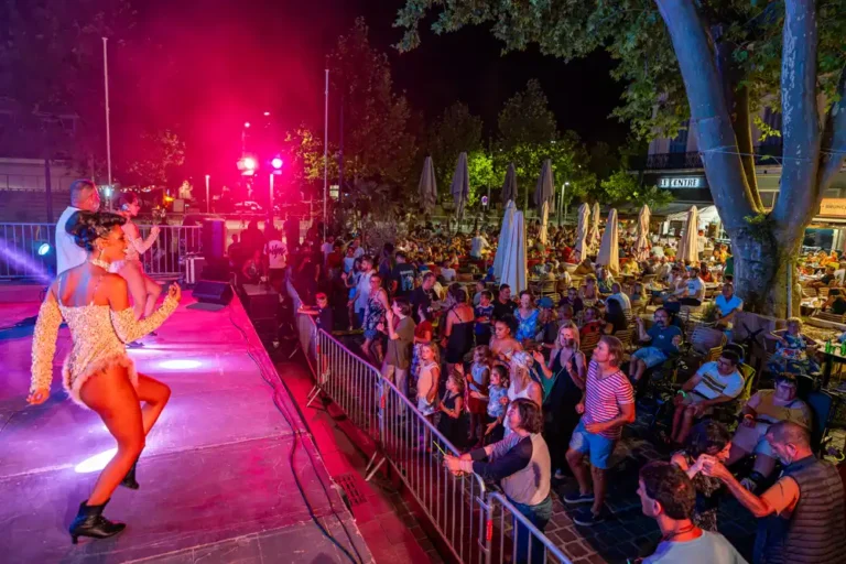 Danseuses sur scène lors d'une soirée festive en extérieur, avec un public nombreux dansant devant la scène.