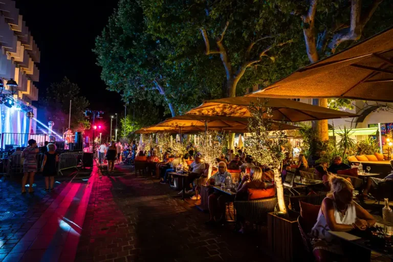 Soirée en extérieur avec terrasse de restaurant animée, éclairages de scène et public lors d'un événement festif nocturne.