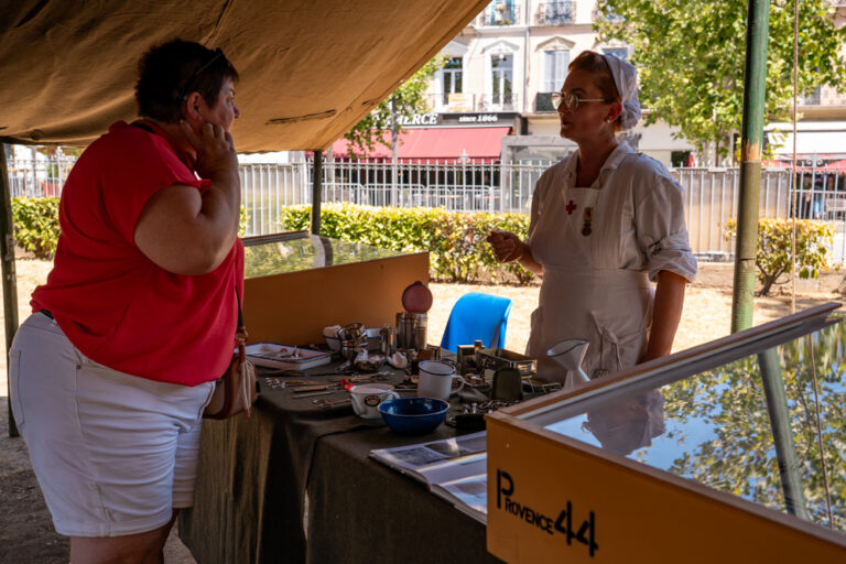 Une femme en tenue d'infirmière militaire d'époque échange avec une visiteuse au sein du camp militaire reconstitué au jardin Anglès.