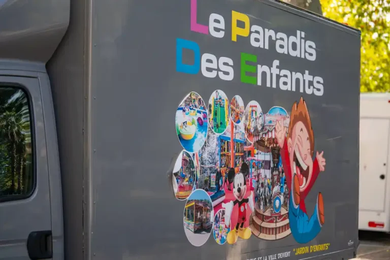 Flanc de camion publicitaire pour la fête foraine, portant l'inscription « Le Paradis des Enfants » et un montage de photos de manèges et d'attractions.