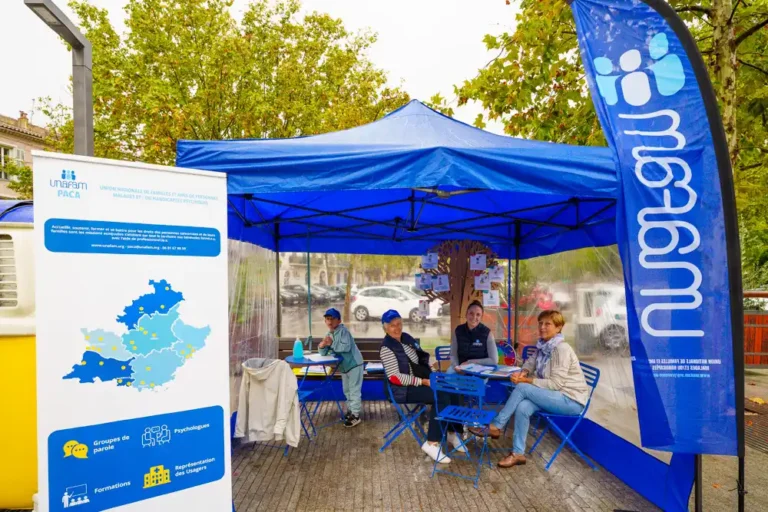 Stand d'information Unafam sous un barnum bleu avec des bénévoles accueillant le public pour parler de santé mentale.